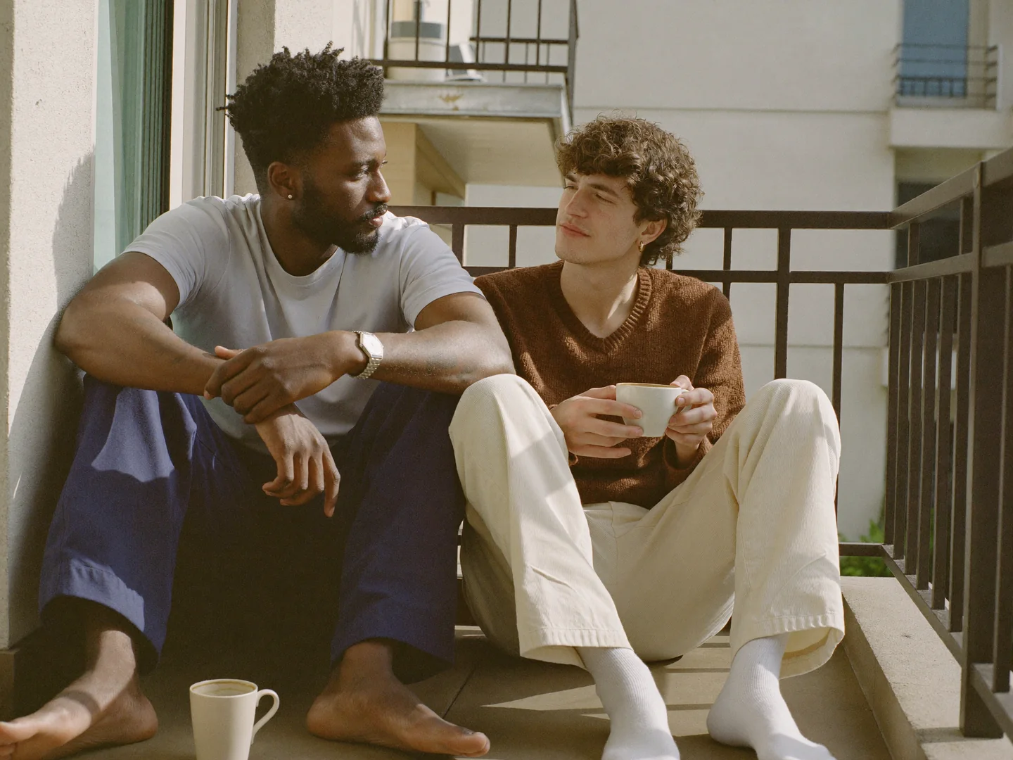Two men sharing coffee together on a balcony.