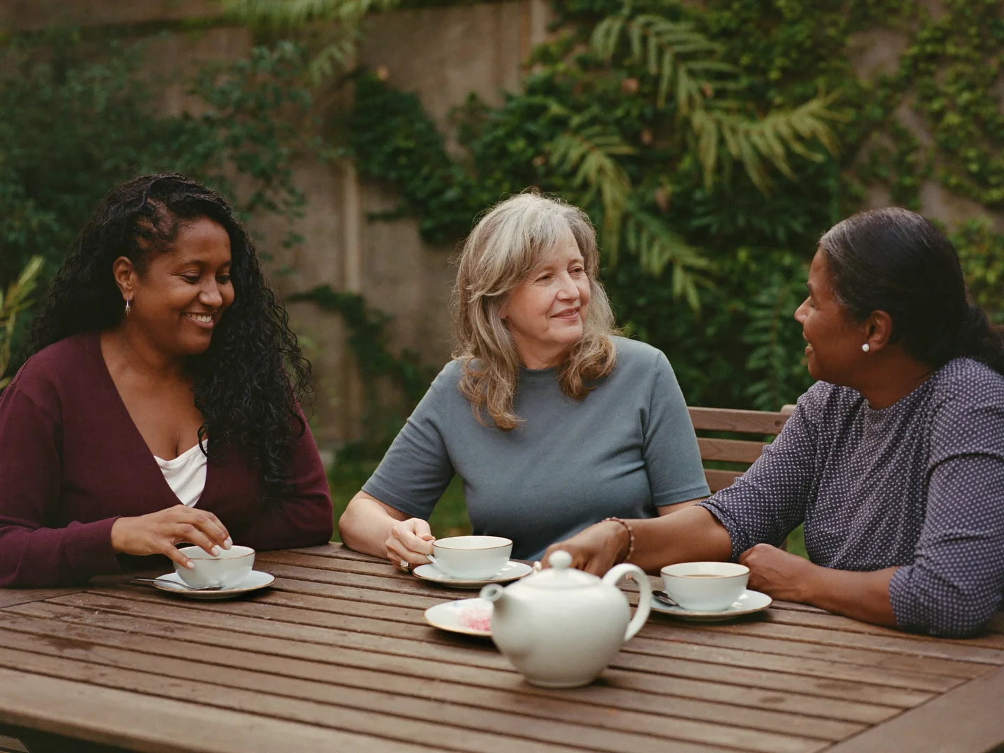 Three women sharing tea and conversation in a garden.