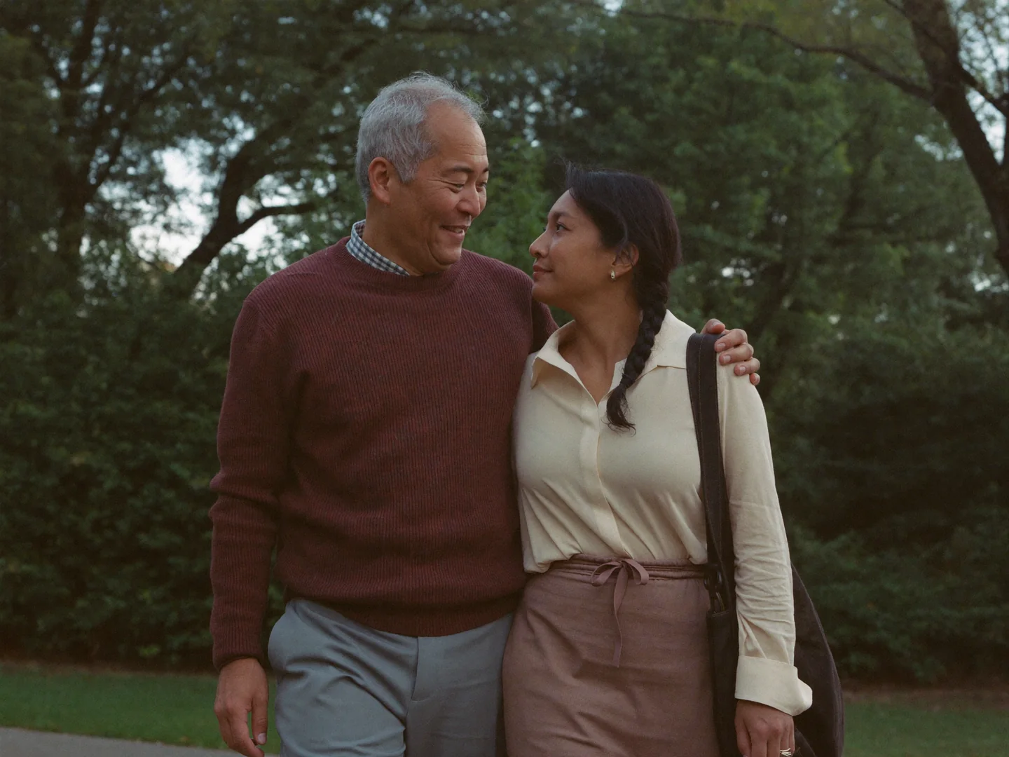 A man and woman walking closely together in a leafy park.